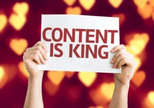 Hænder, der holder et skilt med "Content is King" skrevet på en baggrund af slørede hjerteformer, der illustrerer emneklyngernes magt til at skabe meningsfulde forbindelser og forbedre indholdsstrategien.